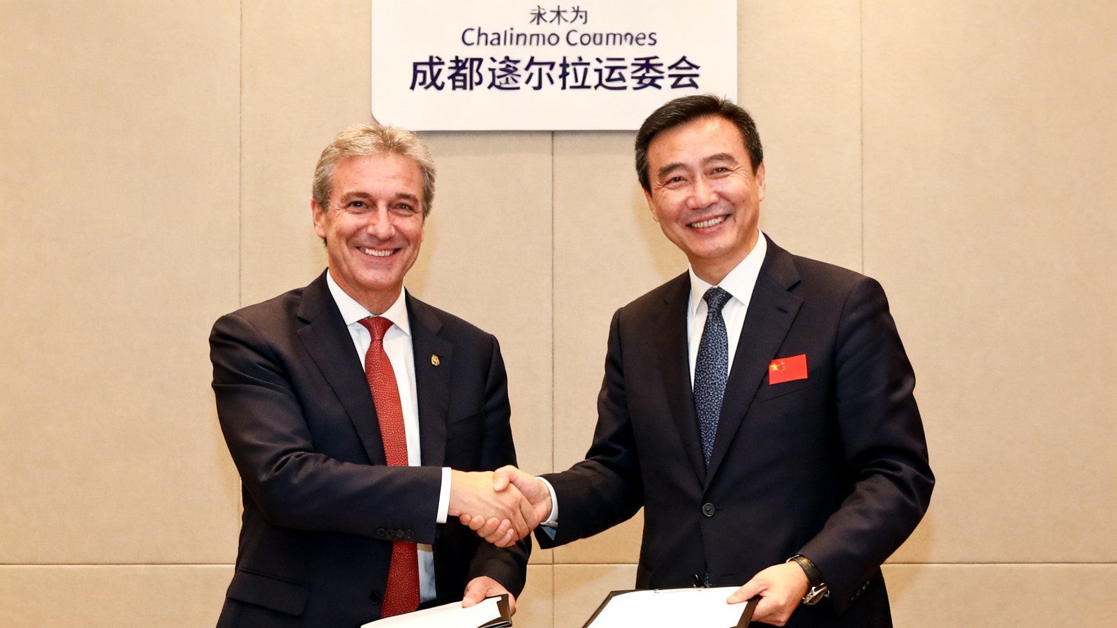 米兰中国代表与成都大运会组委会在签约仪式上握手交换文件的照片，双方代表面带微笑，背景是成都大运会官方会徽。